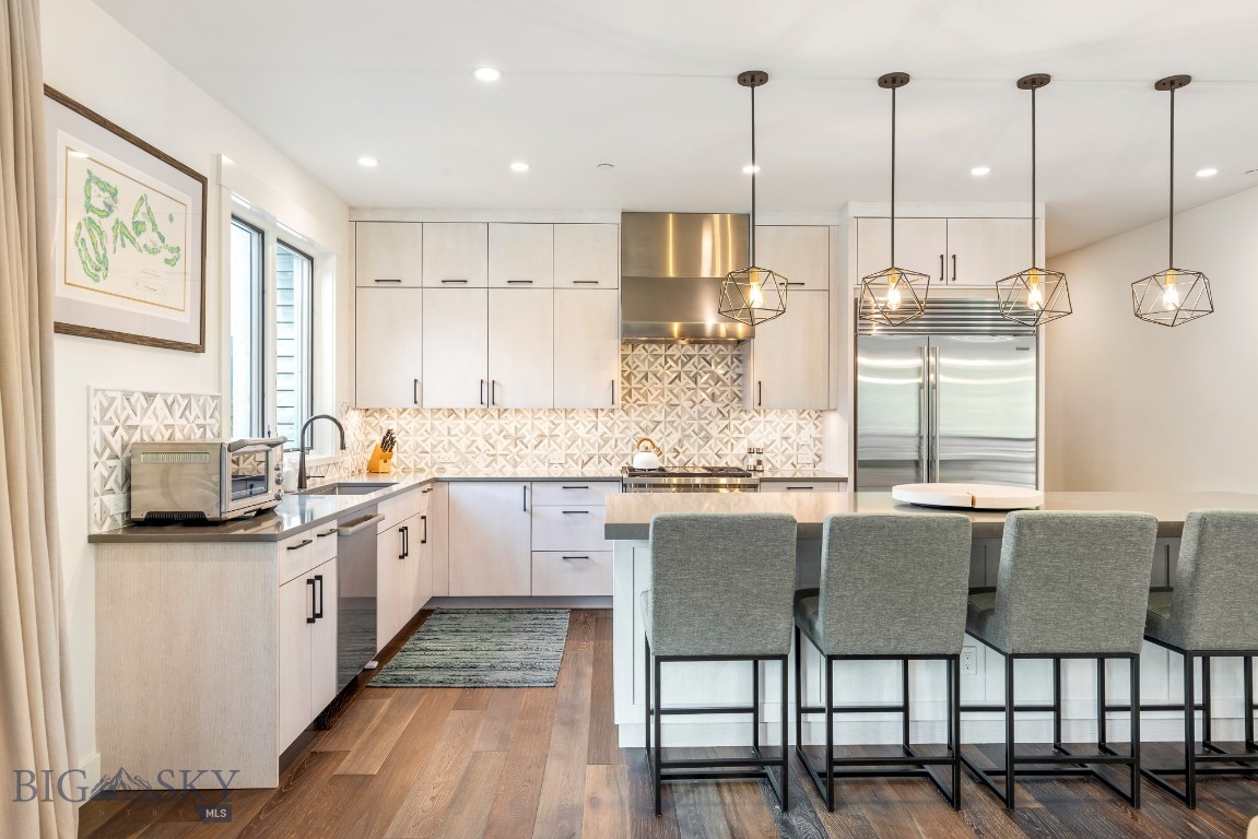Modern kitchen with a large island, patterned backsplash, stainless steel appliances, and geometric pendant lights.