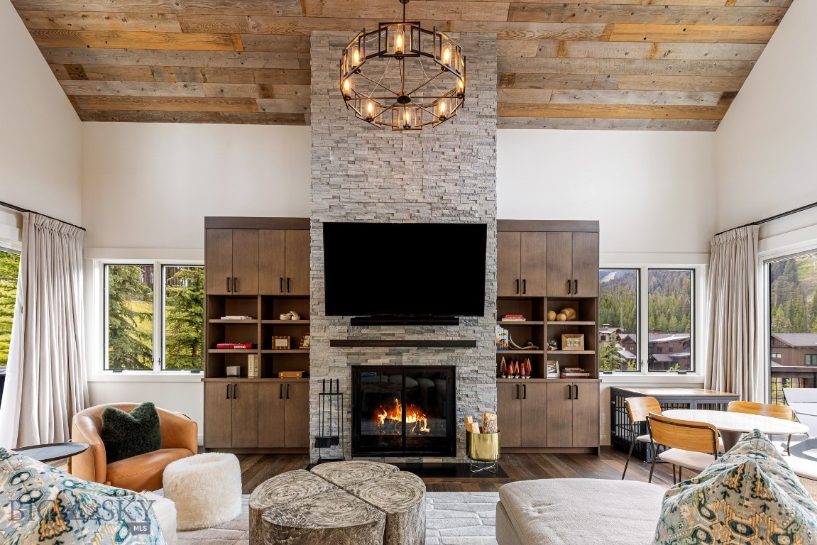 Living room with a stone fireplace, reclaimed-wood ceiling, built-in cabinetry, and forested mountain views.