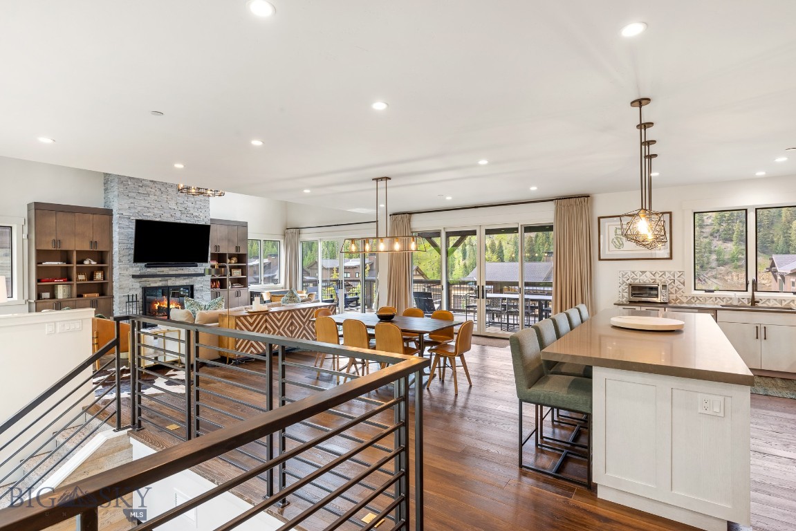 Open-plan kitchen and living area with a large island, stone fireplace, and windows overlooking trees.