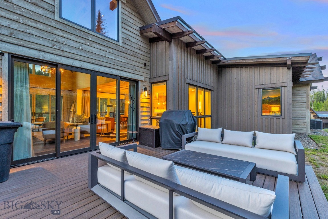 Wood-sided home with a spacious deck, white lounge seating, and glass doors glowing at dusk.