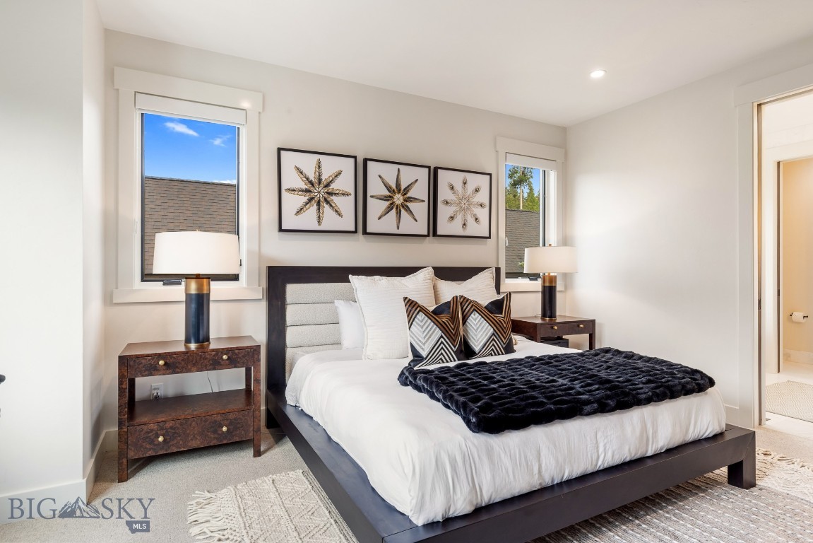 Furnished bedroom with a dark wood bed, white linens, navy throw, and framed botanical prints.