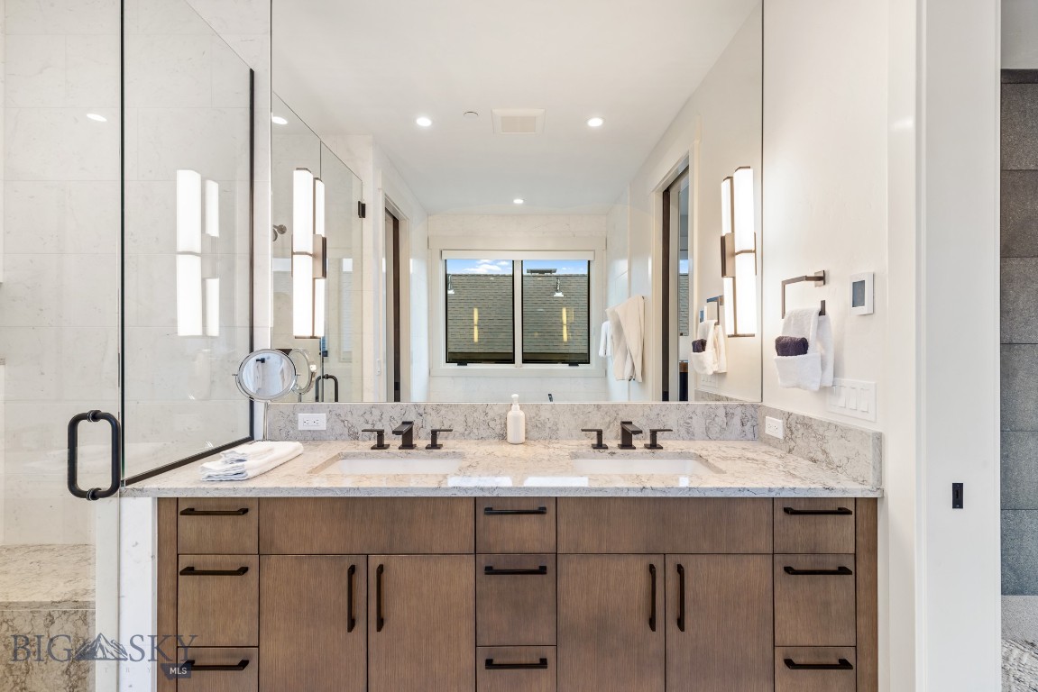 Bathroom with a double-sink wood vanity, marble countertop, and glass shower enclosure.