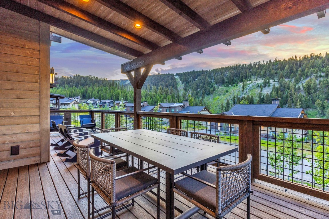 Covered deck with outdoor dining and lounge furniture overlooking a forested mountain hillside.