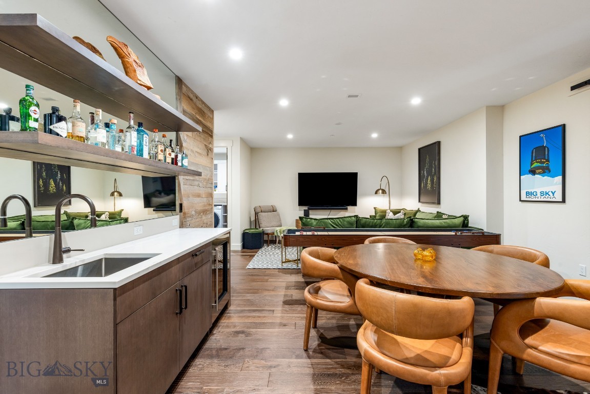 Open-plan living and dining area with a bottle-lined wet bar, round table, leather chairs, and green sofa.