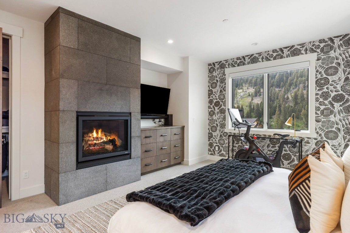Bedroom with a stone fireplace and exercise bike beside a window overlooking forested mountains.