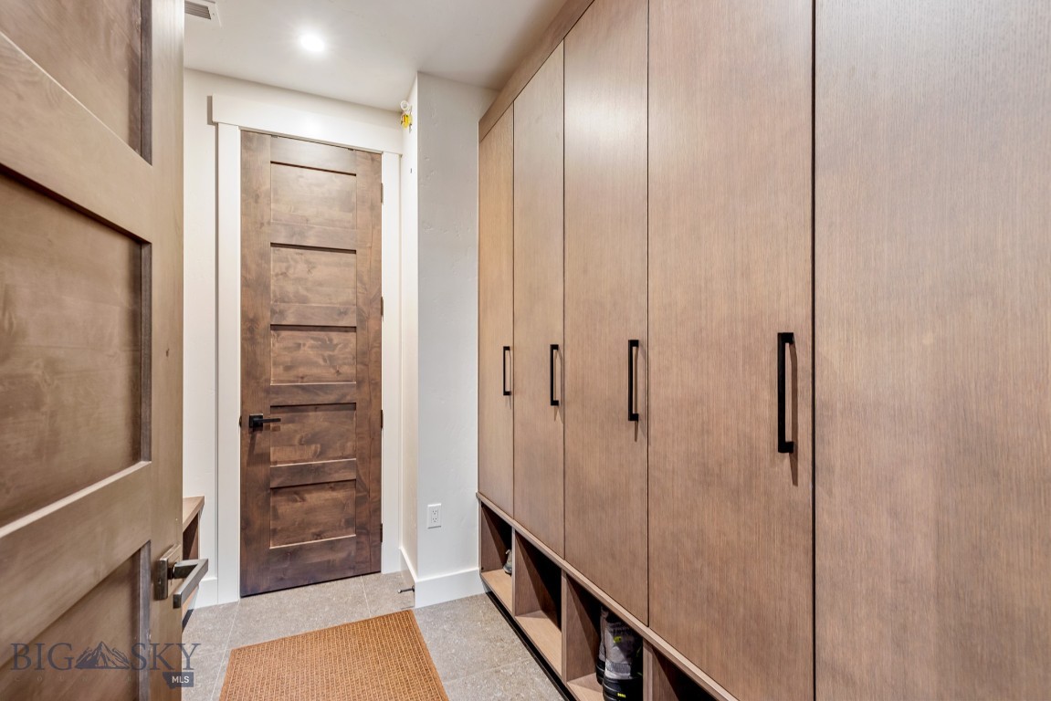Mudroom with light wood cabinets, open shoe cubbies, a woven runner, and a dark paneled door.