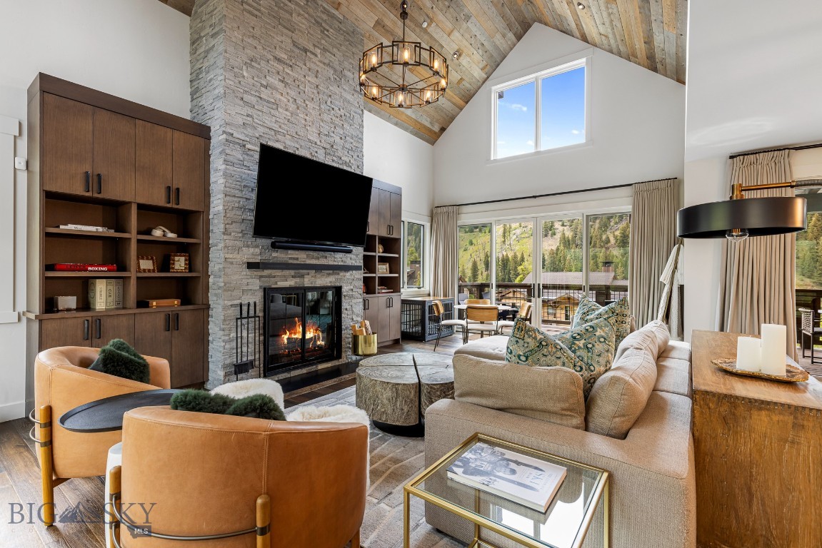Living room with a vaulted wood ceiling, stone fireplace, and windows overlooking wooded mountains.
