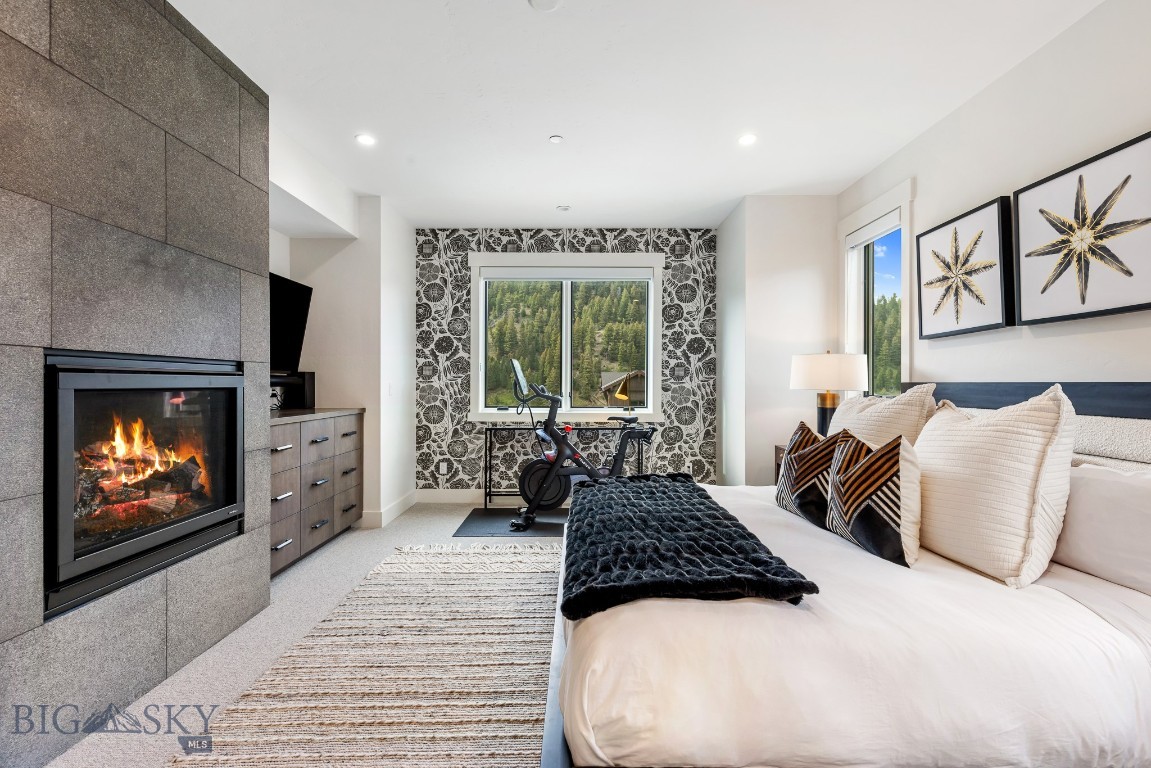 Staged bedroom with a stone fireplace, exercise bike, and forested mountain views.
