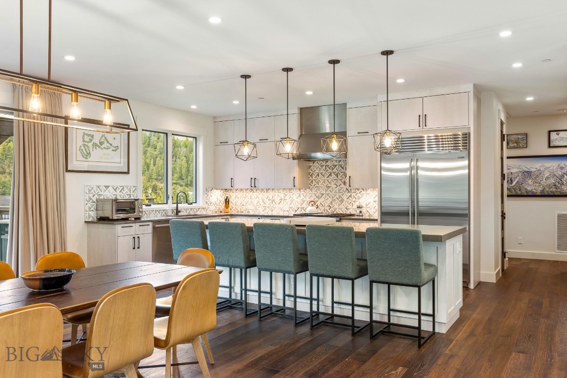 Kitchen with a large island, blue bar stools, patterned tile backsplash, and windows overlooking evergreen trees.
