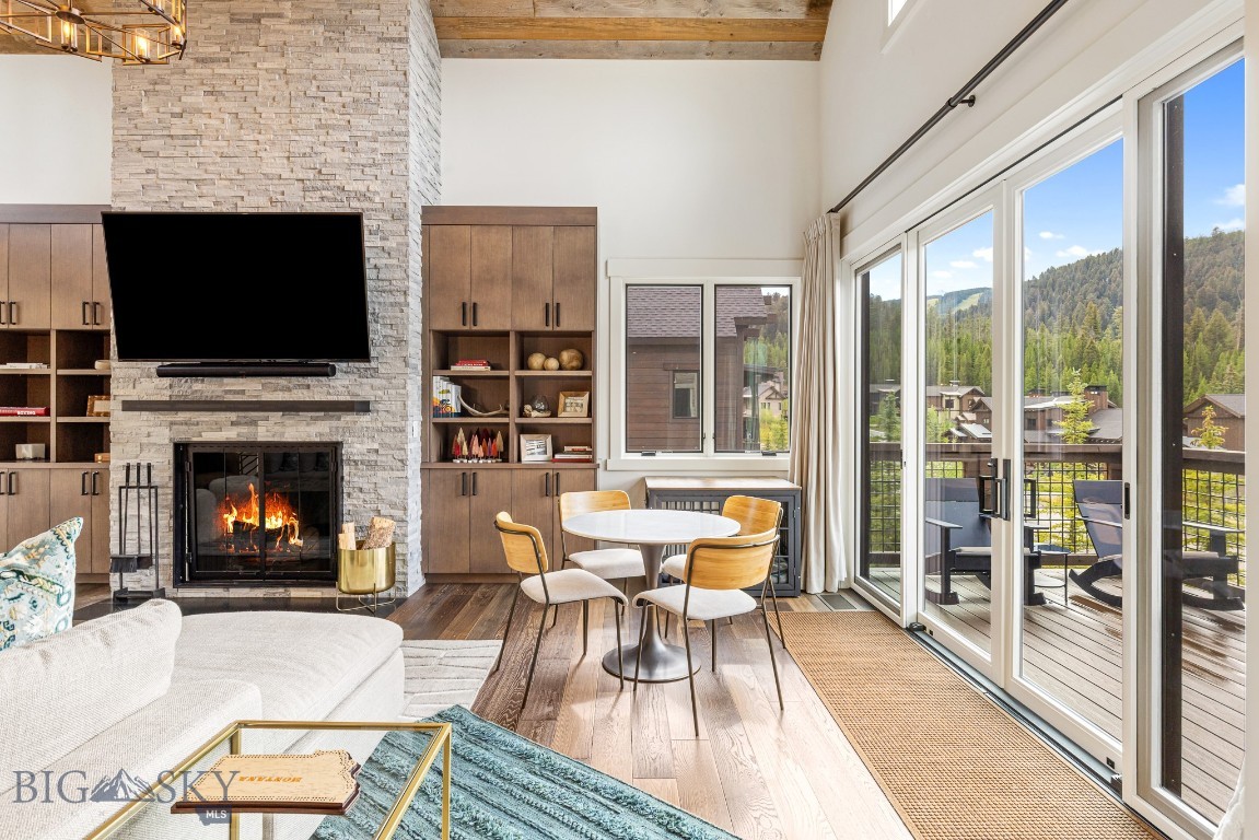 Living room with stone fireplace, dining table, and deck doors overlooking wooded hills.