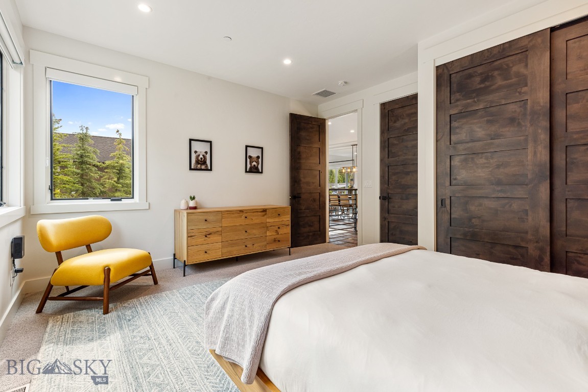 Bedroom with a white bed, mustard-yellow chair, and dark wood doors.