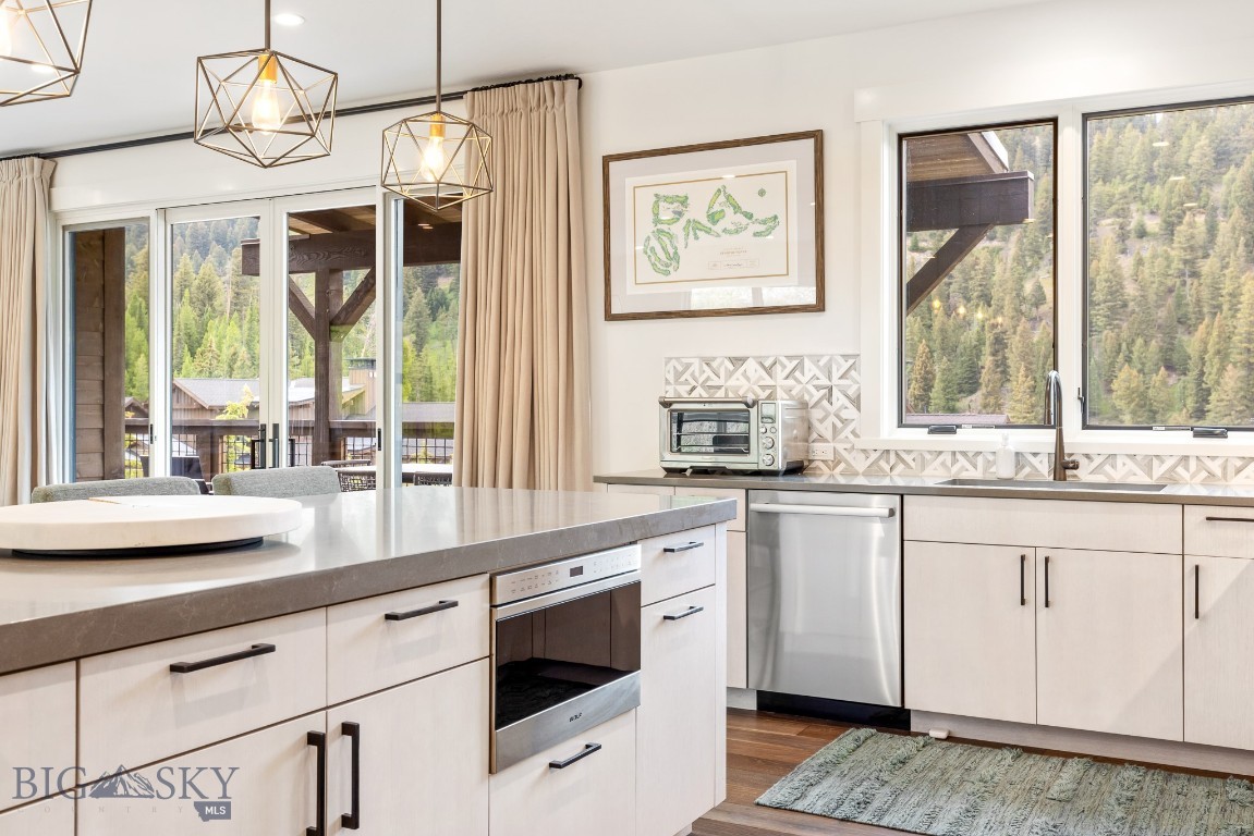 Modern white kitchen with stainless steel appliances and wooded mountain views through large windows.