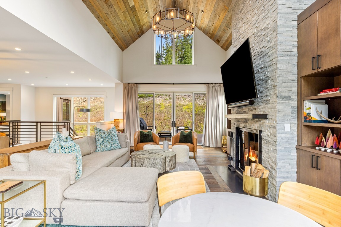 Vaulted living room with a stone fireplace, wood ceiling, and large windows.
