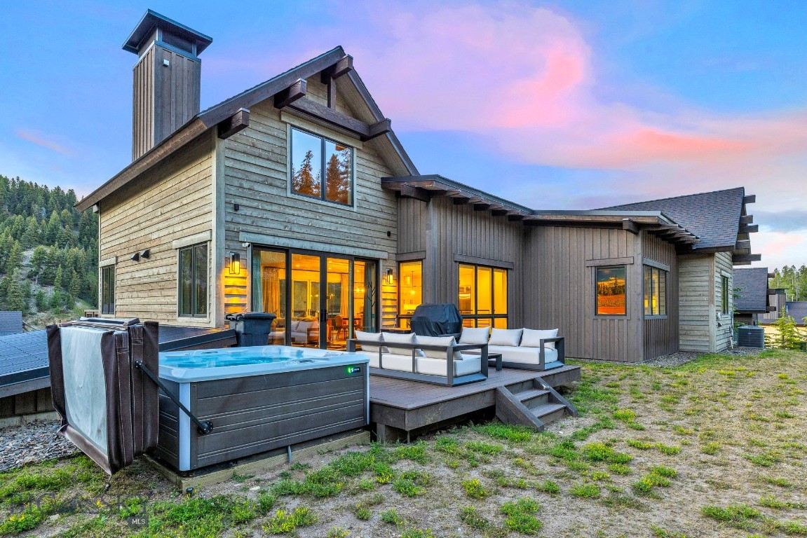 Modern wood-sided home with a raised deck, outdoor seating, and a large hot tub at dusk.
