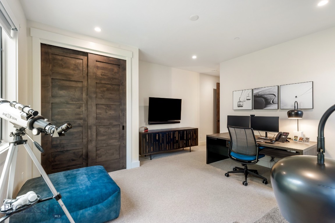 Furnished home office with dark barn doors, dual-monitor desk, wall-mounted TV, and a telescope by the window.