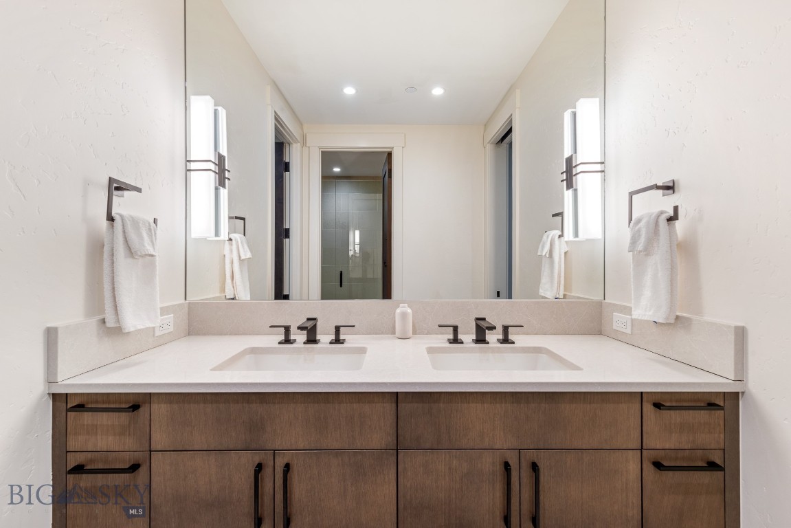 Bathroom double vanity with dark wood cabinets, a pale countertop, and a large mirror.