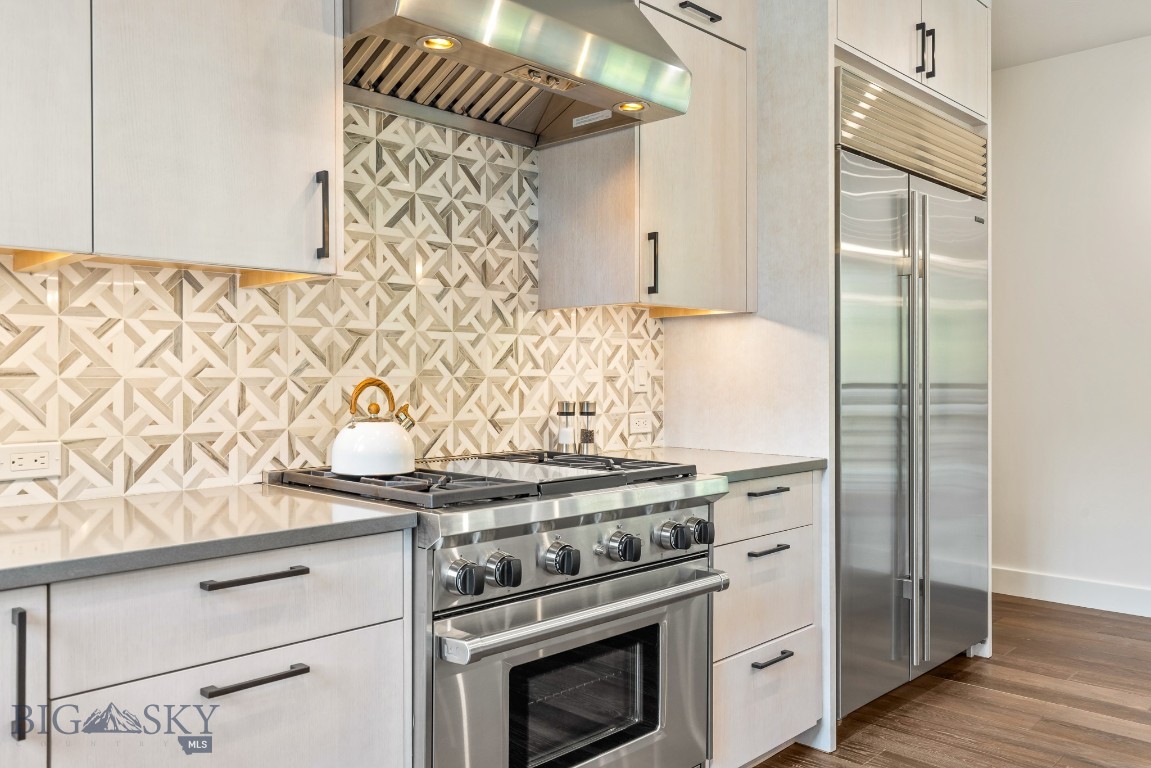 Modern kitchen with geometric tile backsplash, stainless-steel range, and built-in refrigerator.