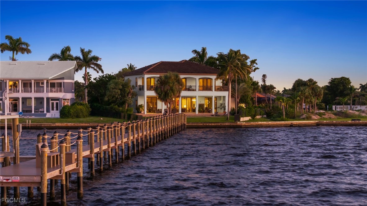 Waterfront home with a red tile roof and palm-lined dock extending into the canal at dusk.