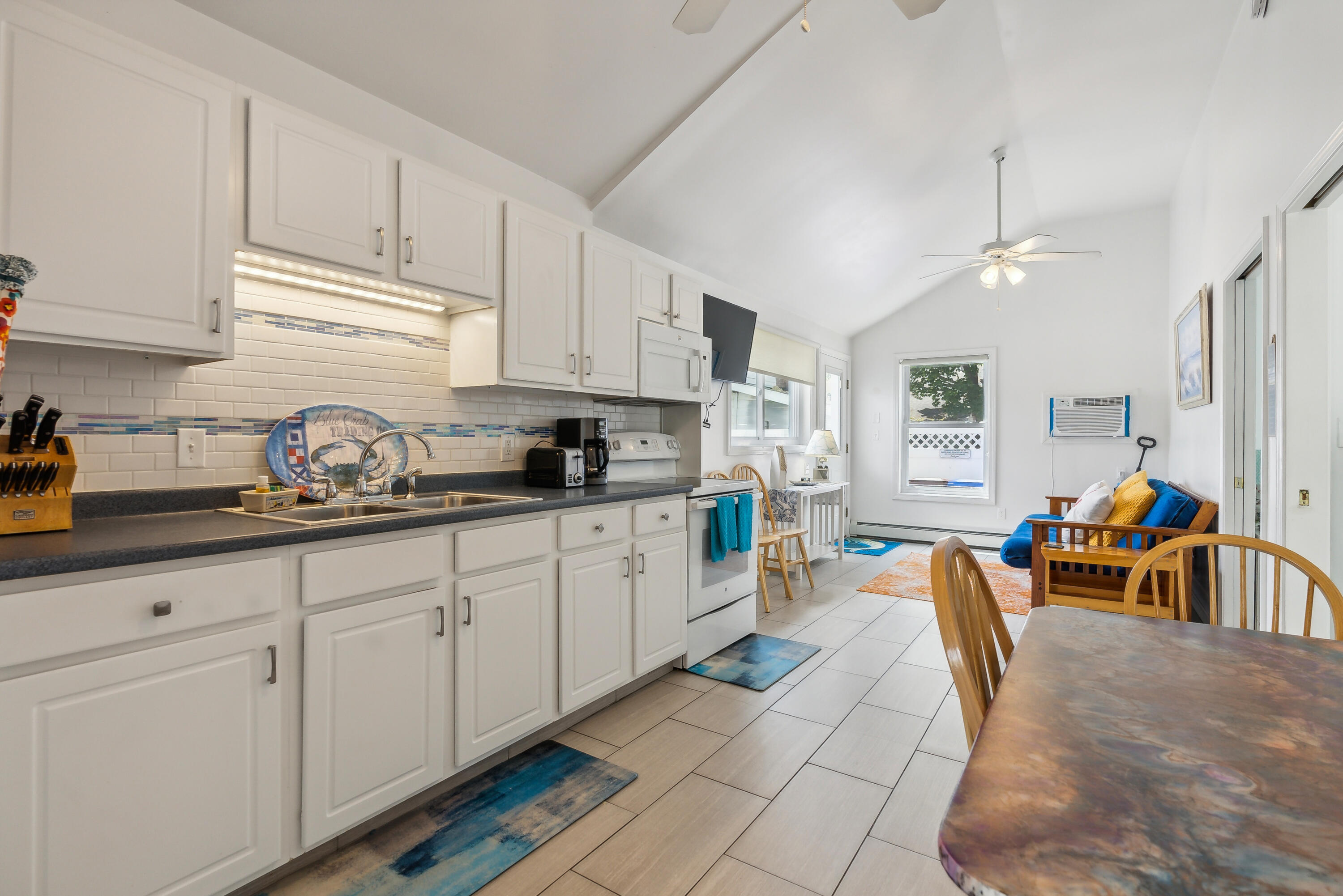 Bright kitchen with white cabinets, tile backsplash, and an open dining and sitting area.