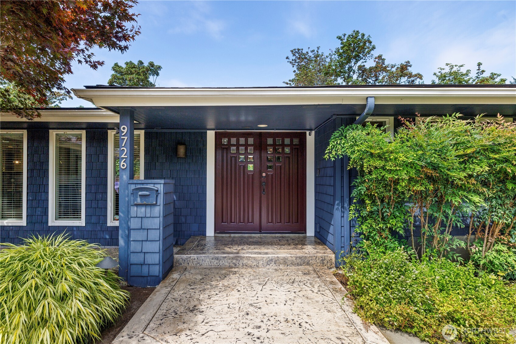 Blue-shingled home entrance with burgundy double doors, stone walkway, and house number 9726.