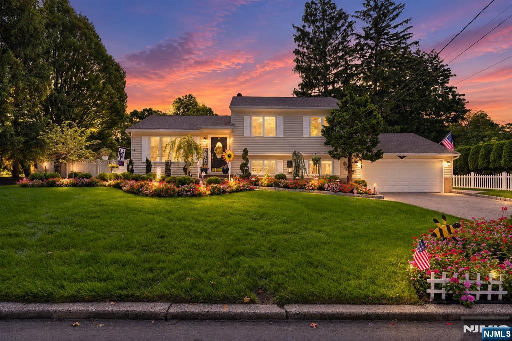 Two-story house with attached garage, flower gardens, and a broad lawn at dusk.