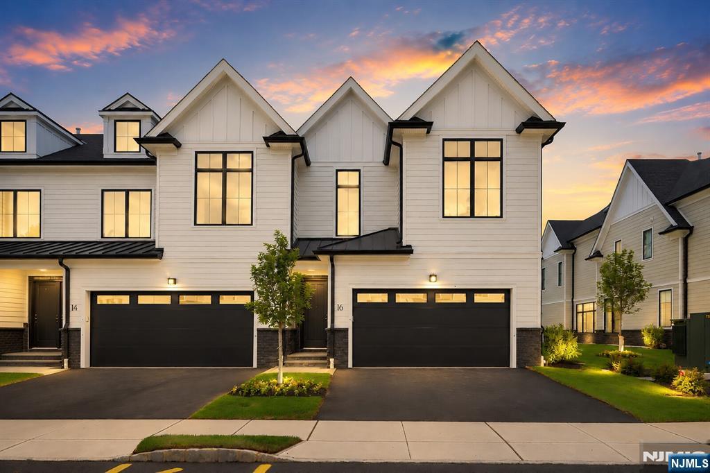 Attached white-sided homes with steep gables and black garage doors at dusk; number 16 is centered.