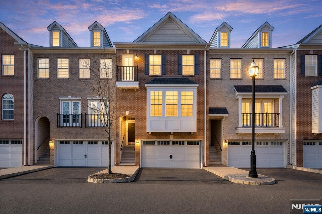 Brick townhouses with attached garages and illuminated windows at dusk.
