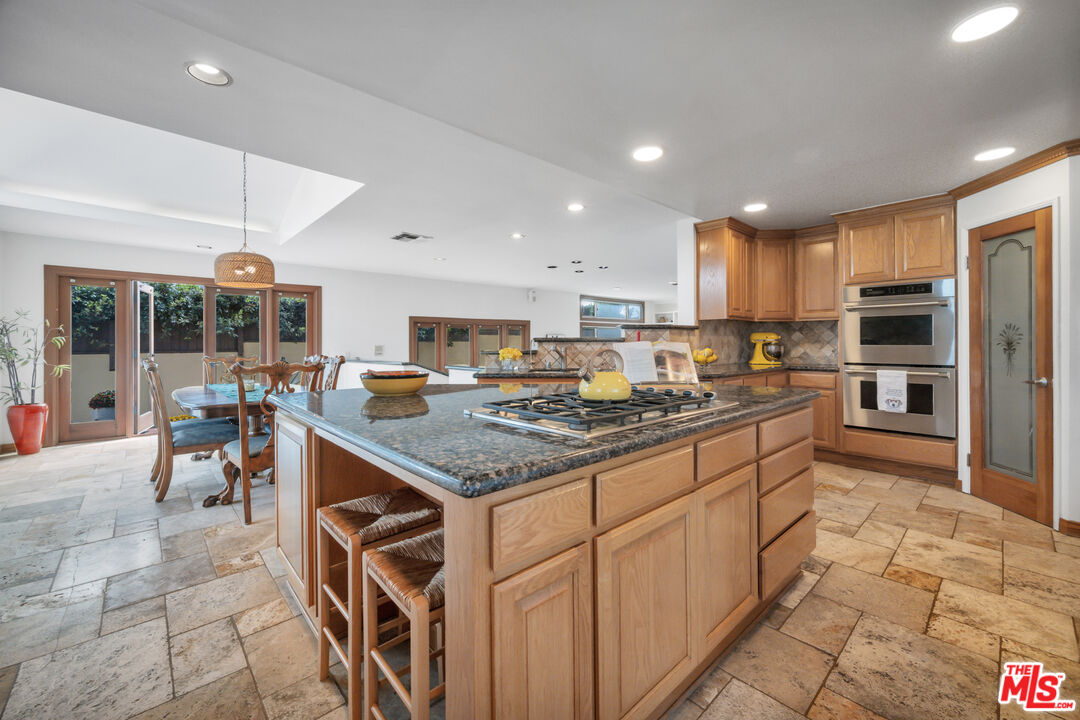 Kitchen with a large granite island, gas cooktop, warm wood cabinets, and adjoining dining area.