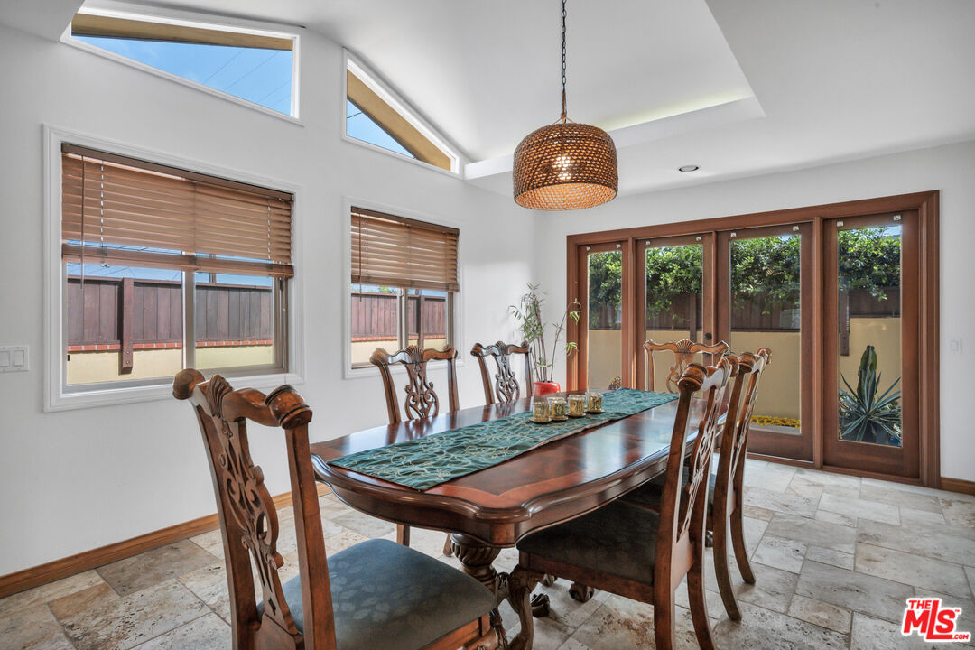 Dining room with a carved wood table, high windows, and garden-facing glass doors.