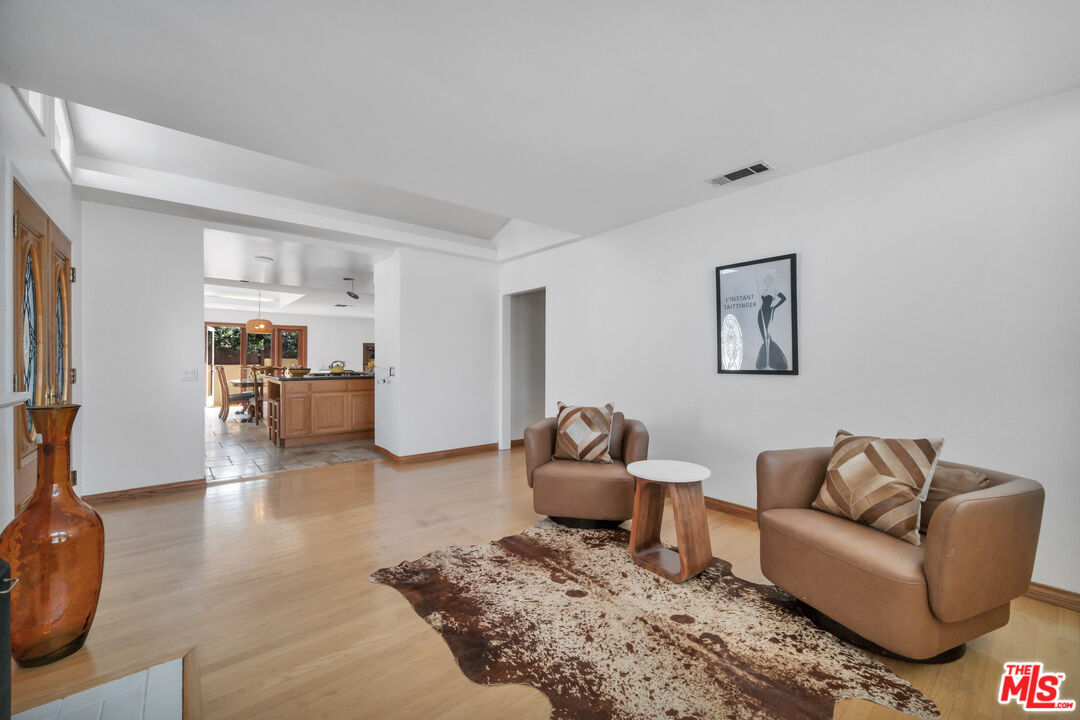 Furnished living room with brown leather armchairs, a patterned rug, and a view into the kitchen.