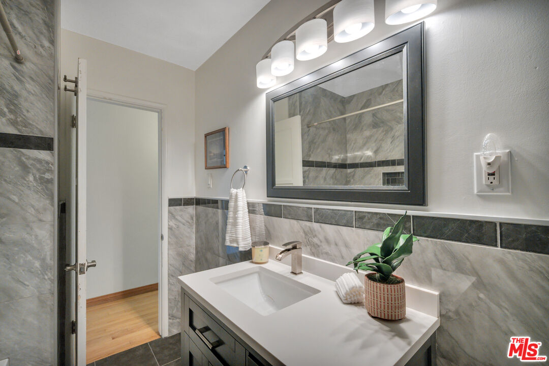 Bathroom with gray marble tile, a white vanity, large mirror, bright lights, and a potted plant.