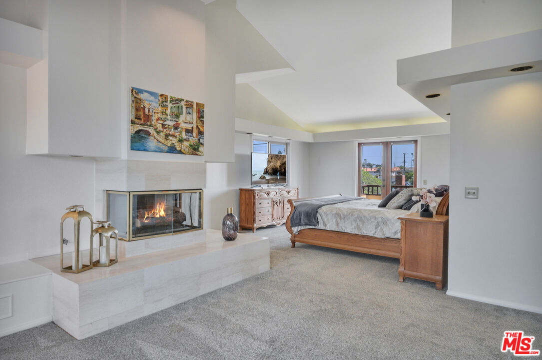 Bedroom with a wooden bed, gray bedding, and a lit fireplace on a white stone hearth.