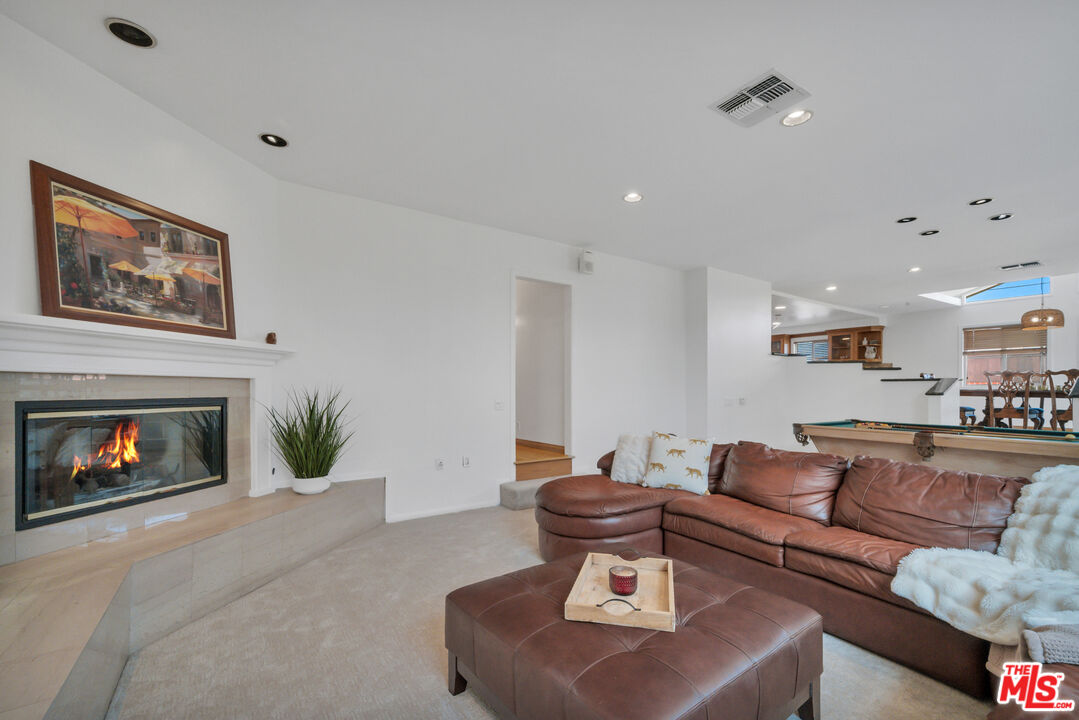 Living room with a leather sectional, lit fireplace, and pool table in the adjoining open-plan space.