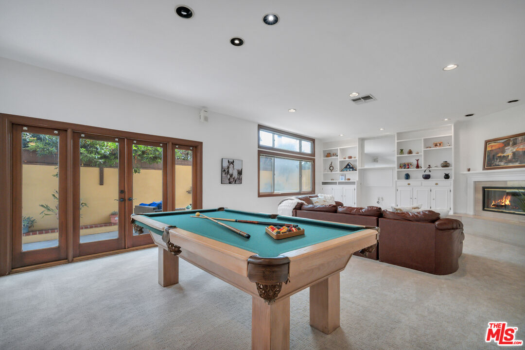 Game room with a green-felt pool table, leather seating, built-in shelves, and a fireplace.
