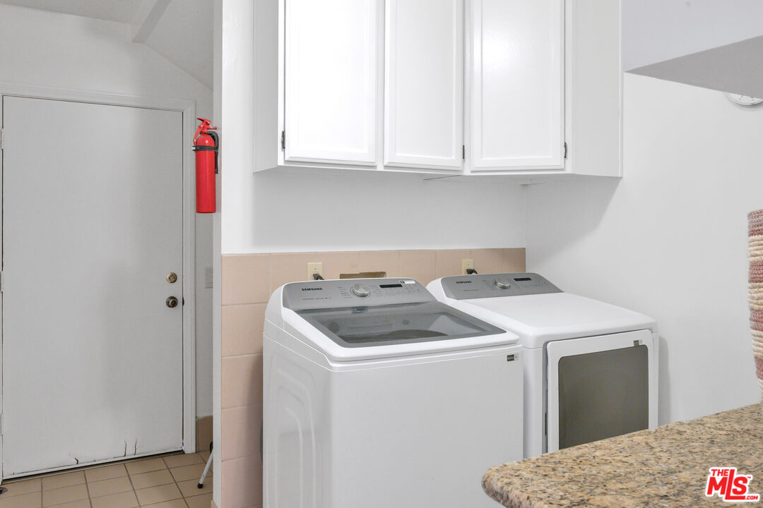 Laundry room with a top-loading washer, dryer, white cabinets, and tiled backsplash.