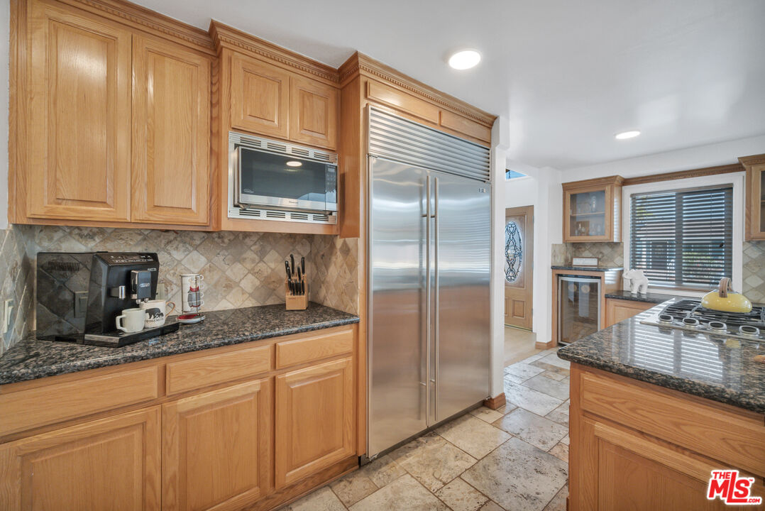 Kitchen with honey-toned wood cabinetry, granite counters, and a stainless steel refrigerator.