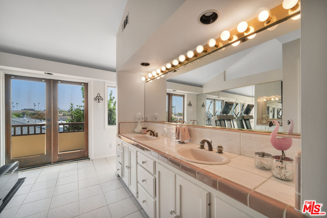 Bathroom with a tiled double-sink vanity, large mirror, globe lights, and balcony doors.