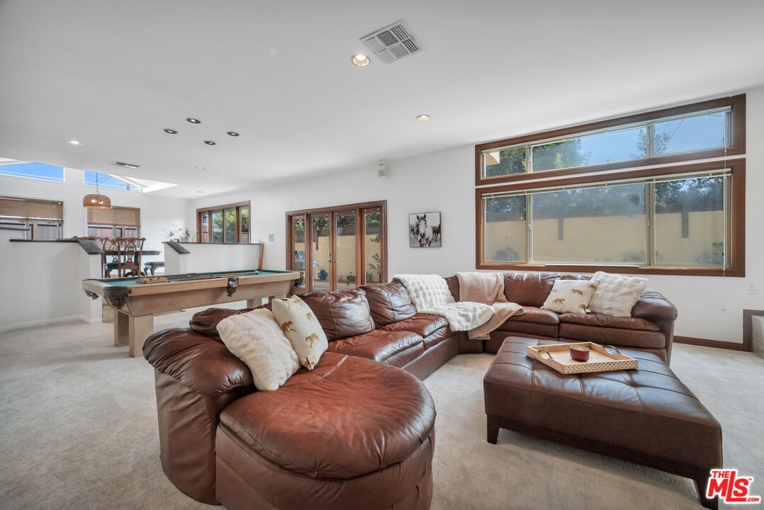 Living and recreation room with a leather sectional, pool table, and large wood-trimmed windows.