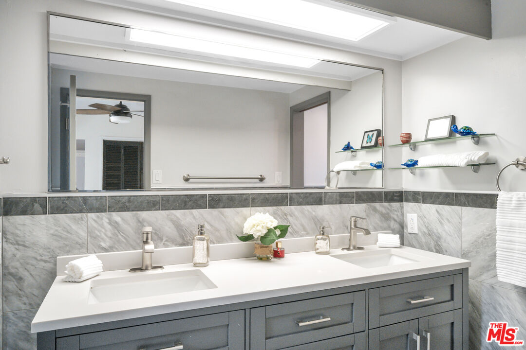 Bathroom with a gray double-sink vanity, marble-patterned tile, and a large mirror.