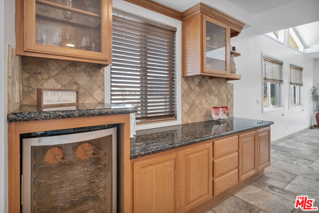Kitchen with wood cabinetry, dark granite counters, and a built-in wine refrigerator.