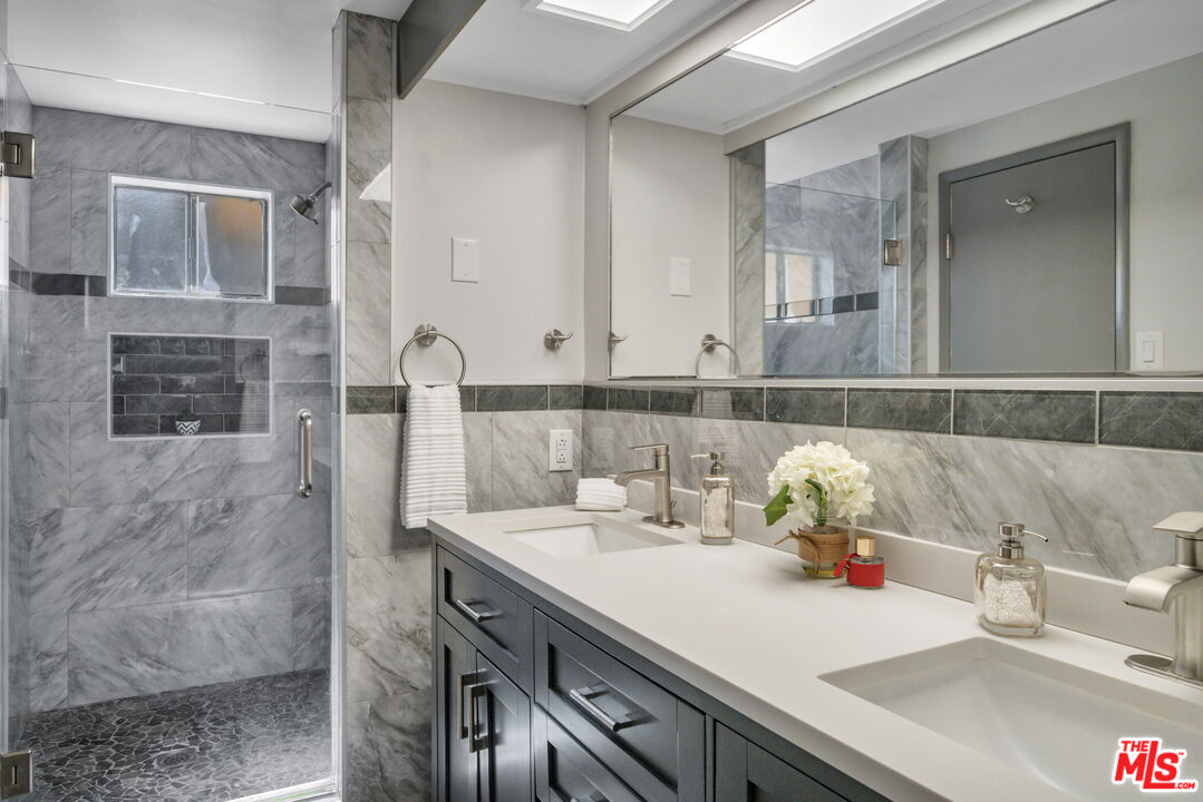 Bathroom with gray marble tile, glass walk-in shower, and long double vanity.