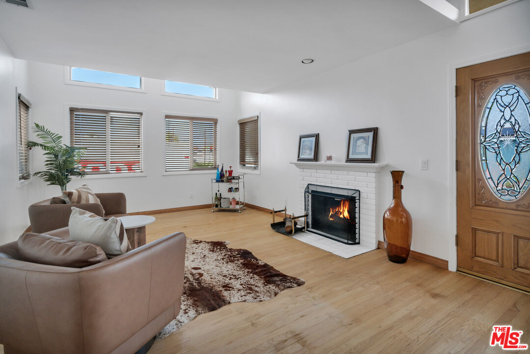 Living room with a white brick fireplace, brown seating, hardwood floors, and a stained-glass entry door.
