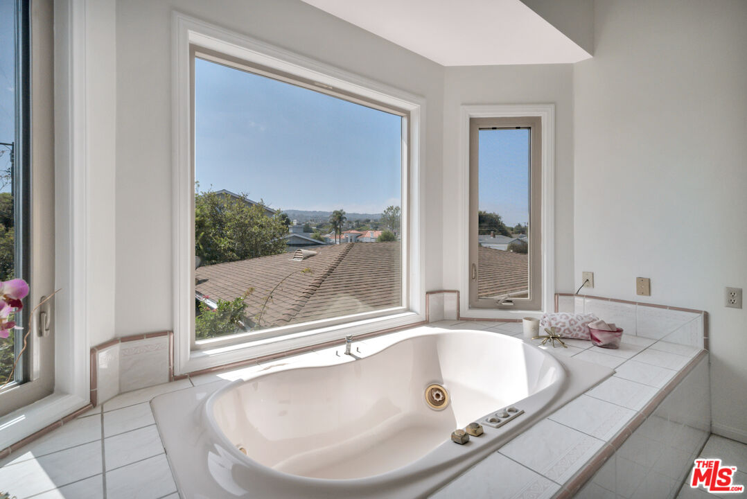 Corner soaking tub beneath large windows overlooking rooftops and trees.