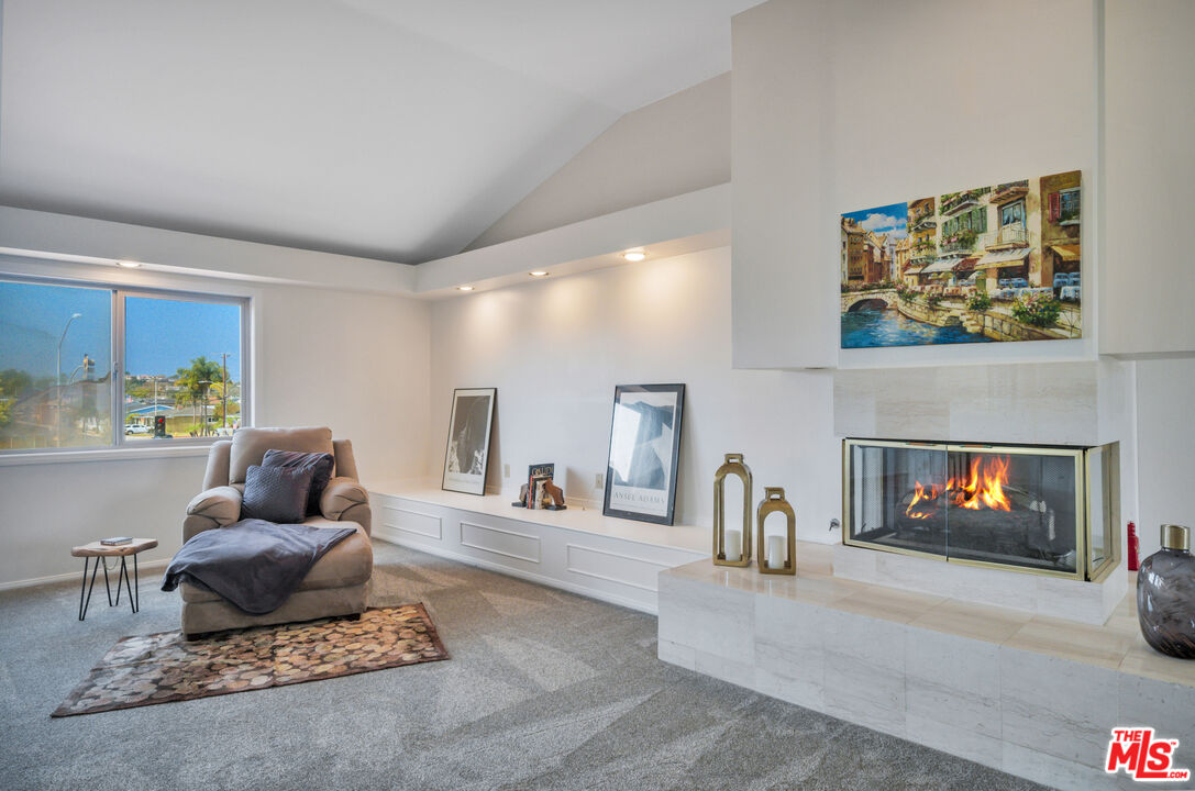 Living room with a vaulted ceiling, marble fireplace, and large window.