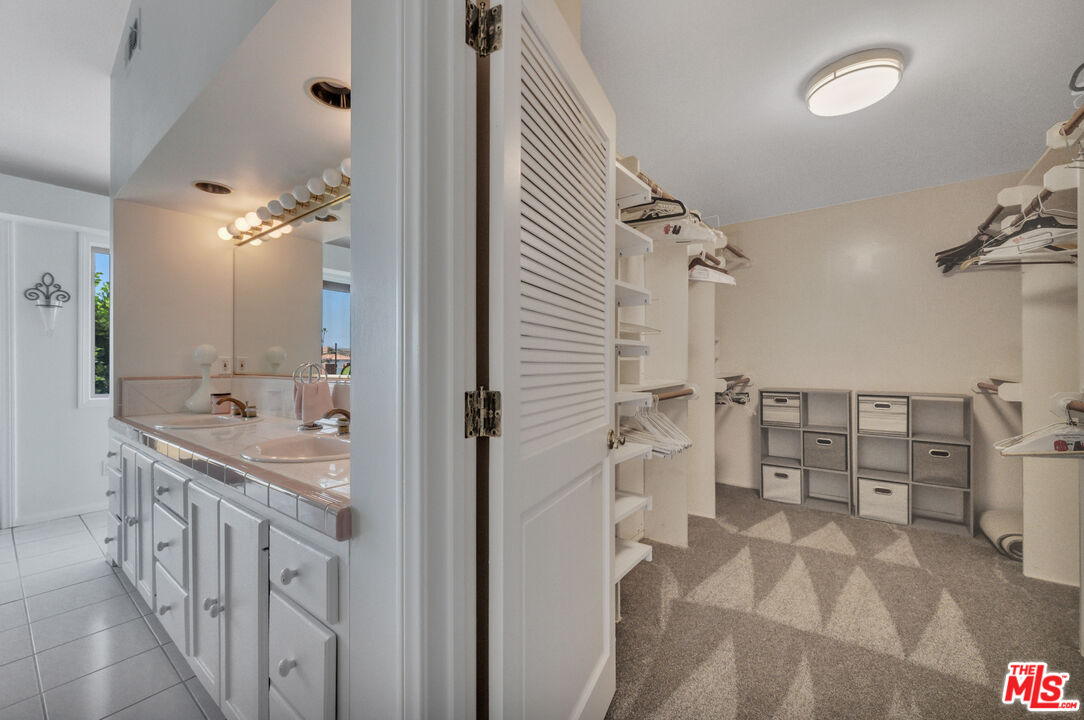 Bathroom vanity beside a walk-in closet with built-in shelves and storage bins.