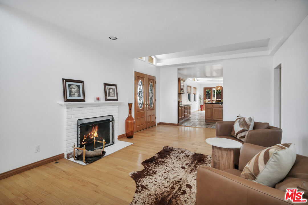 Living room with a white brick fireplace, wood floors, brown seating, and a cowhide rug.
