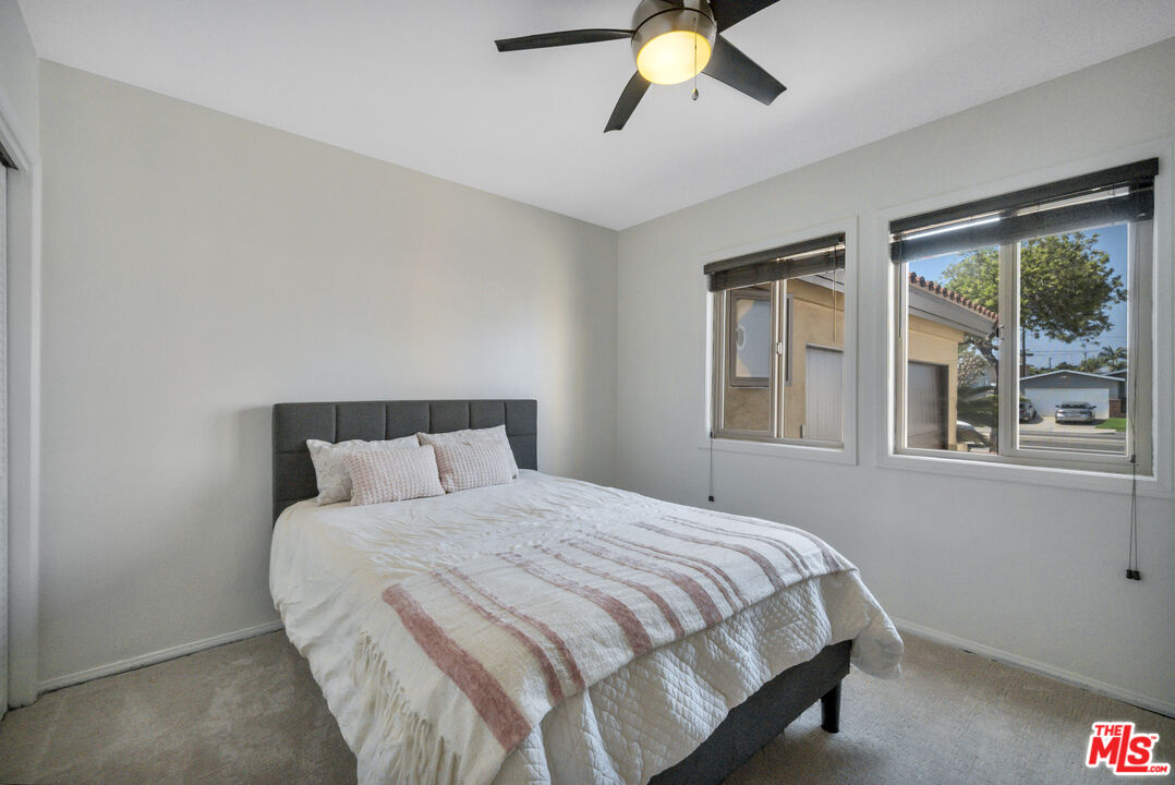Bedroom with a white-and-pink striped quilt, dark headboard, ceiling fan, and two windows.