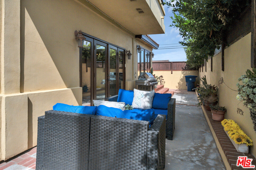 Side patio with wicker seating, blue cushions, glass doors, and a barbecue grill.