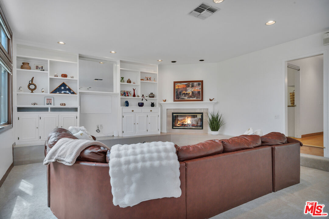 Living room with a brown leather sectional, white built-ins, and a lit fireplace.