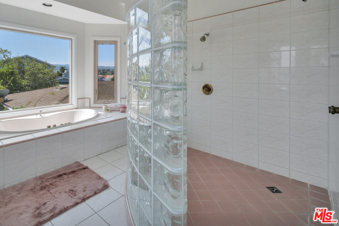 Tiled bathroom with a window-side soaking tub and a glass-block-enclosed shower.